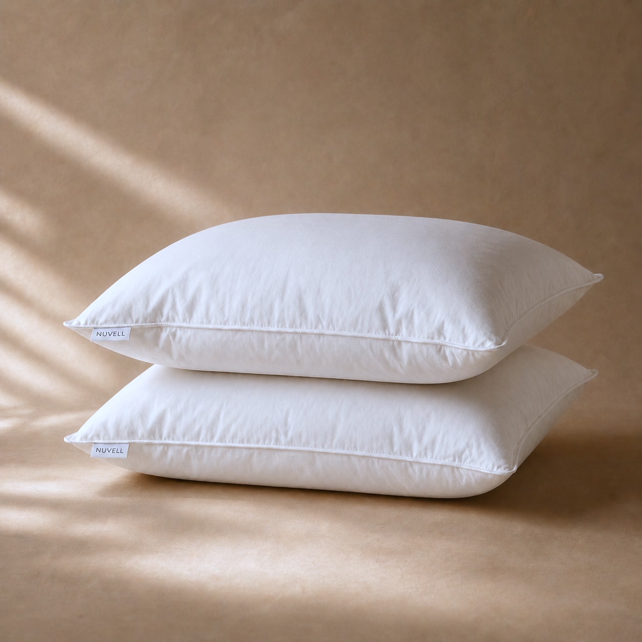 Two white NUVELL pillows on a warm neutral surface